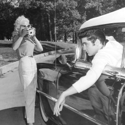 Elvis Presley lehnt sich aus einem Fahrzeugfenster und wird dabei von zwei Frauen fotografiert.