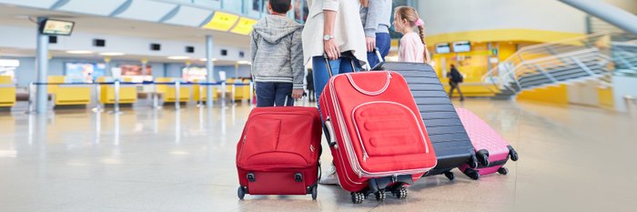 Familie mit Kindern zieht am Flughafen Koffer hinter sich her. 