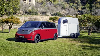 Elektrischer VW ID Buzz zieht einen Anhänger über eine grüne Wiese. 