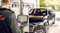 Mann steht an Diagnosegerät vor einem Auto.