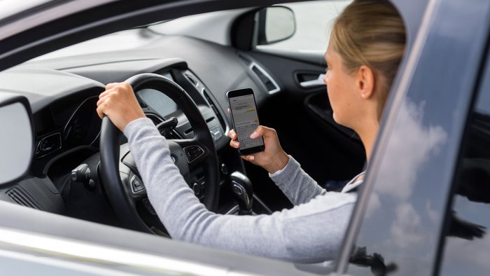 Junge Frau im Auto tippt auf dem Handy. 