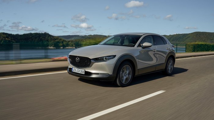 Ein Mazda CX-30 fährt bei Sonnenschein auf einer Straße 