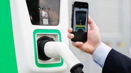 Ein Mann scannt den QR-Code an einer Ladesäule mit seinem Smartphone.. 