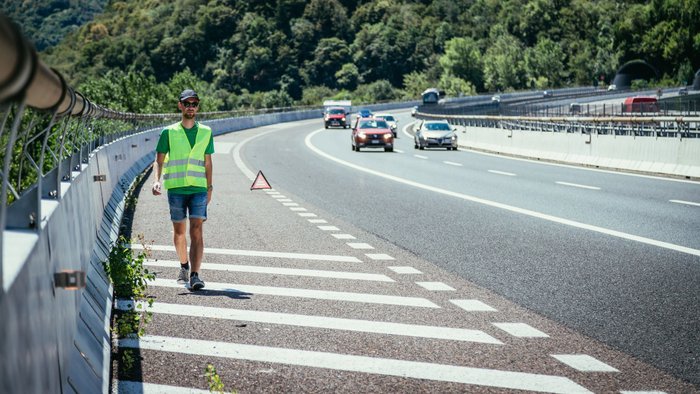 Mann mit Warnweste läuft auf dem Seitenstreifen einer Straße entlang. 