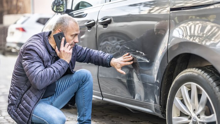 Mann begutachtet Schaden an seinem Auto. 