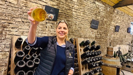 Junge Frau hält in einem Weinkeller eine Flasche in die Höhe.