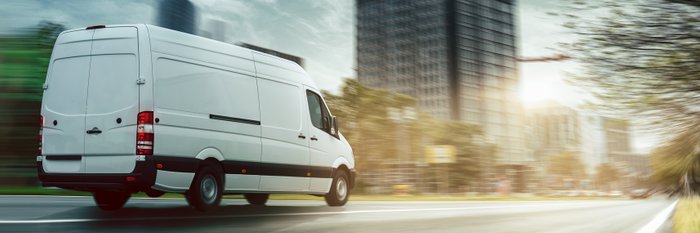 weißer Transporter, der in einer Stadt fährt.