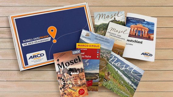 Ein ARCD-Urlaubspaket, daneben Reiseführer und Broschüren über die Mosel auf Holz.