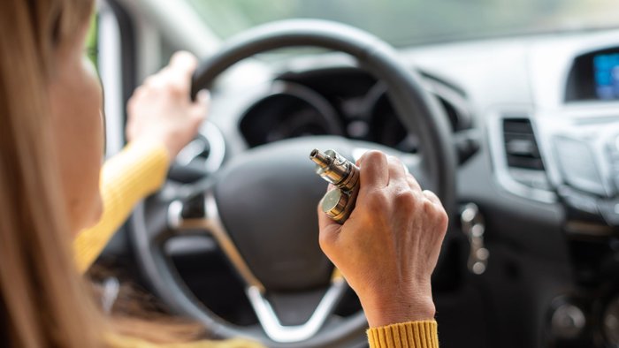 Ältere Frau raucht E-Zigarette beim Autofahren.