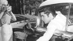 Elvis Presley lehnt sich aus einem Fahrzeugfenster und wird dabei von zwei Frauen fotografiert.