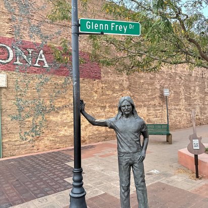 Statue von Glenn Frey an einer Straßenlaterne mit nach ihm benannten Straßenschild und Backsteinmauer im Hintergrund.