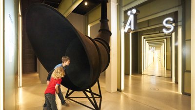 Kinder stecken in einem Museum ihre Köpfe in einen überdimensionalen Trichter.