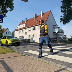 Eine Fußgängerin überquert im Altersanzug einen Zebrastreifen.