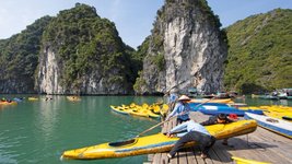 Männer ziehen auf einem Steg ein Boot an Land, im Hintergrund viele weitere Boote im türkisblauen Wasser und hohe begrünte Felsen.
