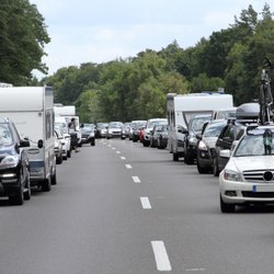 Autos und Wohnwagen stehen bei der Fahrt in den Urlaub auf einer Autobahn im Stau.