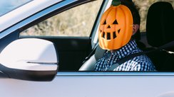Ein Mann sitzt mit einer Halloween-Maske verkleidet am Steuer eines Autos.