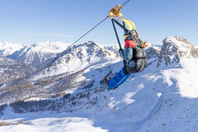 Skifahrer fährt im Skigebiet Mont Serre Chevalier vor verschneiter Bergkulisse eine Zipline hinunter.