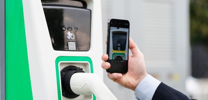 Ein Mann scannt den QR-Code an einer Ladesäule mit seinem Smartphone.. 