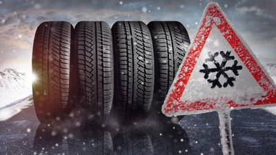 Ein Verkehrsschild mit einer Schneeflocke vor 4 Winterreifen.