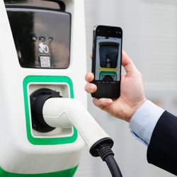 Ein Mann scannt den QR-Code an einer Ladesäule mit seinem Smartphone.. 