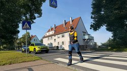 Eine Fußgängerin überquert im Altersanzug einen Zebrastreifen.