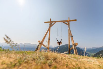 Person schaukelt auf einem riesigen Schaukel-Gestell mit Blick in die Berge.