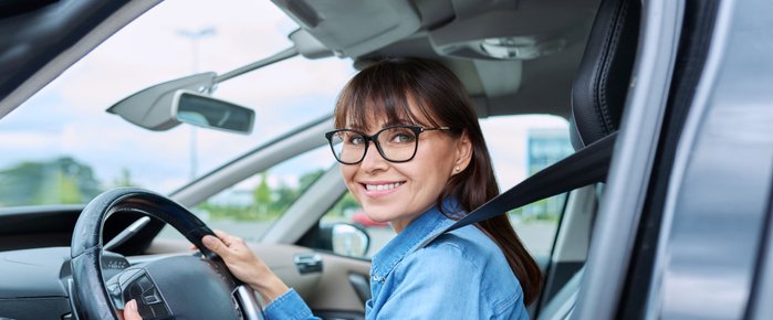 Junge Autofahrerin mit Brille blickt aus Fahrzeugfenster.