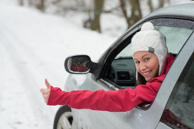 Eine Frau sitzt im Auto und zeigt einen Daumen nach oben in einer verschneiten Landschaft.