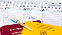 Eine Impfspritze liegt auf einem Impfpass und einem Reisepass.  