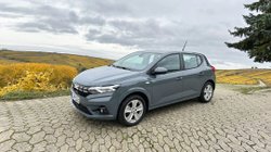 Ein graues Auto auf einem Parkplatz, im Hintergrund Felder und Wiese.