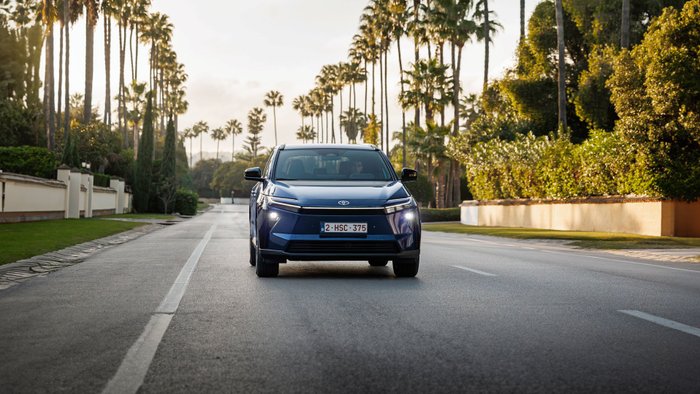 Der Toyota bZ4X auf einer Straße mit Palmen-Allee. 
