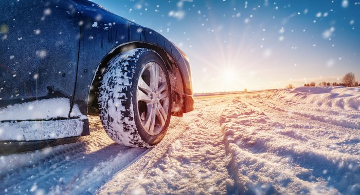 Vorderachse eines Autos mit Winterreifen auf schneebedeckter Straße bei Sonnenschein.