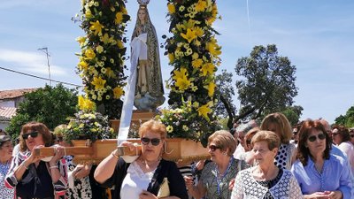Frauen tragen Marienfigur mit Blumenschmuck durch eine Straße.