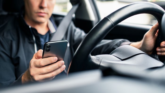 Mann benutzt ein Smartphone während der Fahrt im Auto und ist vom Verkehrsgeschehen abgelenkt.