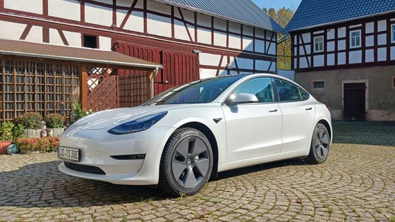 Ein Tesla Model 3 steht vor einer Fachwerk-Scheune.