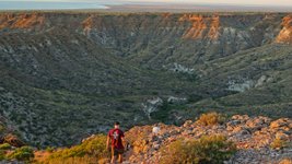Zwei Wanderer laufen durch eine zerklüftete Tiefebene, dahinter das Meer.