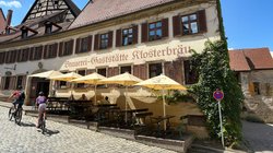 Alte Brauerei-Gaststätte mit Tischen vor dem Gebäude, an der zwei Radfahrer vorbeifahren.