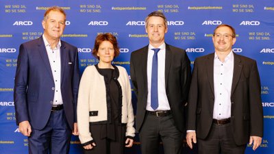 Drei Männer und eine Frau des ARCD-Präsidiums stehen vor eine Wand mit ARCD-Logo.