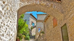 Verwinkelte Dorfgasse mit Steinhäusern, Torbögen und Pflanzen.