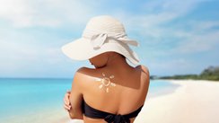 Frau mit Bikini und Sonnenhut am Strand. Auf dem Rücken eine aus Sonnencreme aufgemalte Sonne.