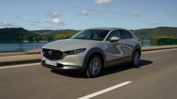 Ein Mazda CX-30 fährt bei Sonnenschein auf einer Straße 