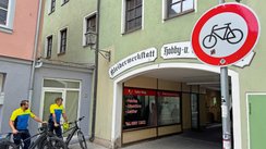 Zwei Polizisten stehen an einem Durchgang und kontrollieren Radfahrer. 