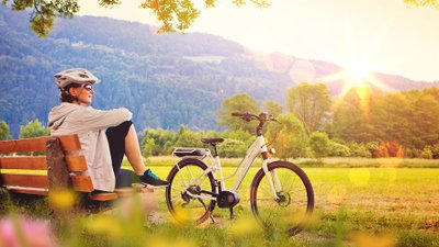 Radfahrerin macht Rast in grüner Landschaft.