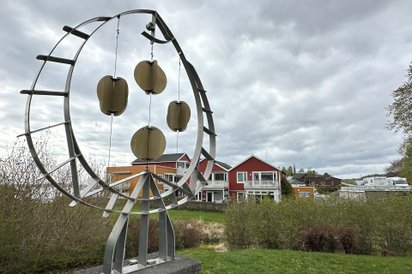 Installation aus Metall in Fischform, im Hintergrund skandinavische Holzhäuser