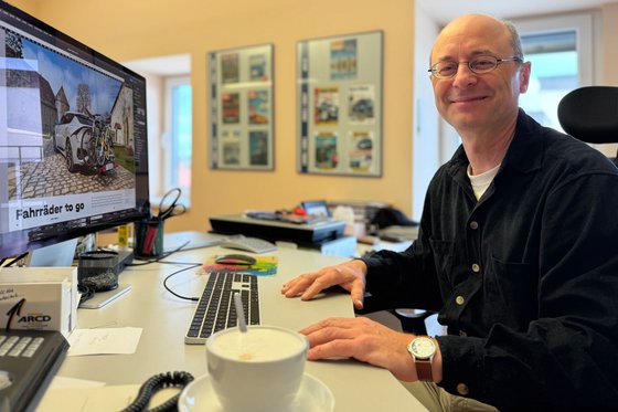 ARCD-Grafiker Horst Holler sitzt am Schreibtisch. 