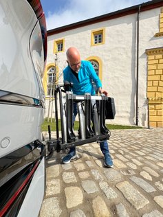 Mann montiert Fahrradträger auf Anhängerkupplung eines Fahrzeugs. 