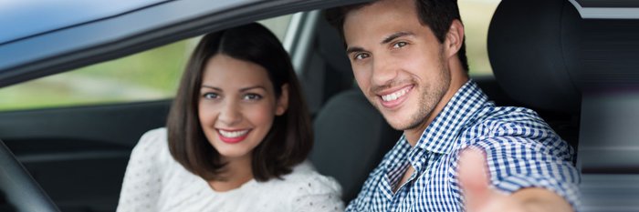 Ein Paar lacht auf den Autofenster, Mann hält Daumen nach oben.