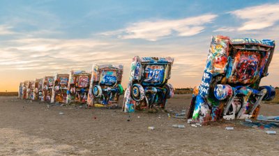 Mit bunten Graffiti besprühte Cadillacs in einer Reihe ragen aus einem wüstenhaften Boden.