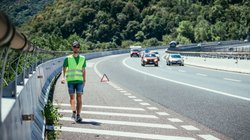 Mann mit Warnweste läuft auf dem Seitenstreifen einer Straße entlang. 