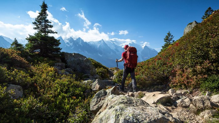 Mann mit Rucksack wandert auf Gebirgspfad; schneebedeckte Gipfel am Horizont.